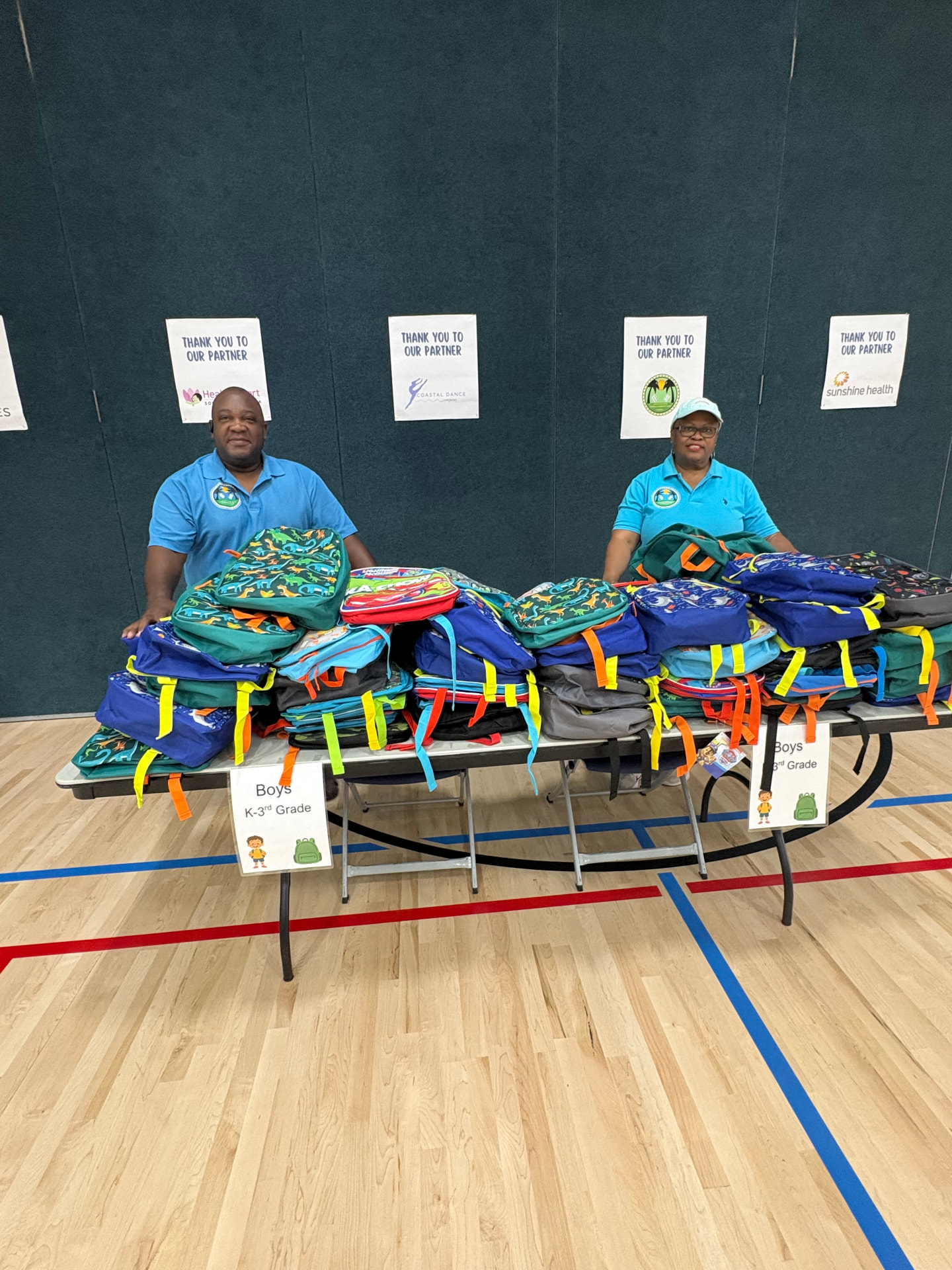 Volunteers behind a table stacked with donated backpacks