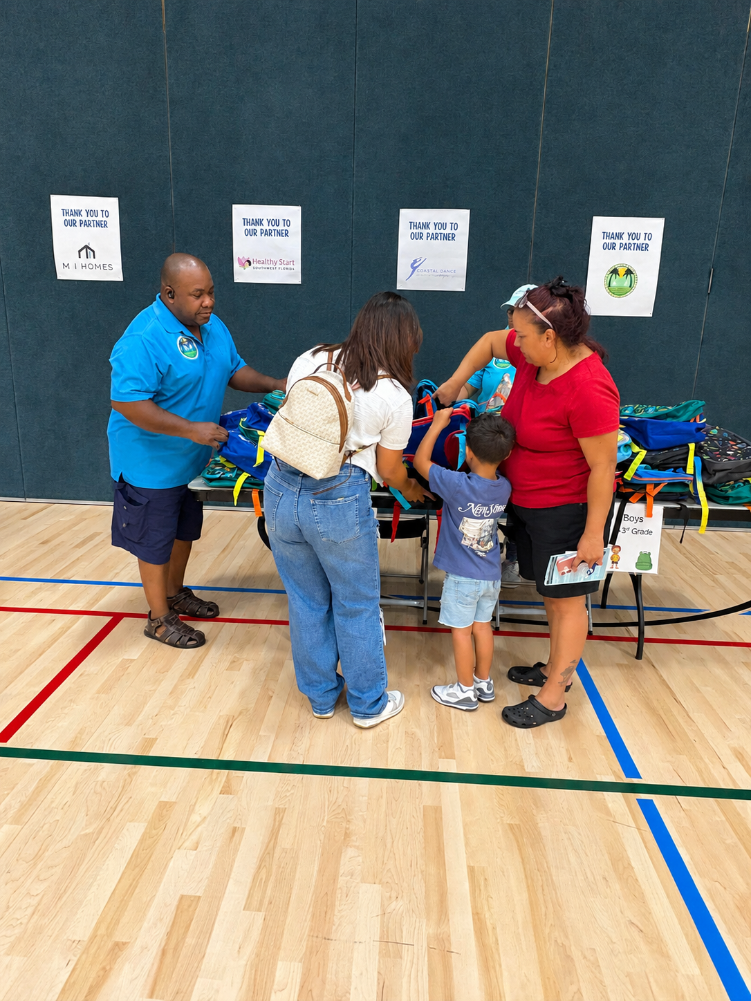 Volunteer helping a family select backpacks in the gym