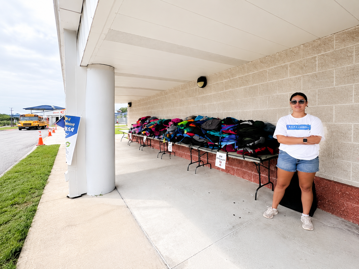 Volunteer standing next to tables filled with donated backpacks for the school supply drive
